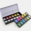 Open case of colorful watercolor pans arranged in two rows on a white background.